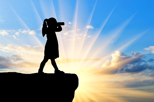 Silhouette of baby girl standing on top, looking through binoculars. The concept of children's discoveries and adventures