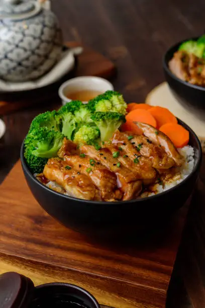 Japanese Food Style : Top view of Homemade Chicken Teriyaki grilled with rice , carrot , broccoli put on the black bowl and place on wooden table
