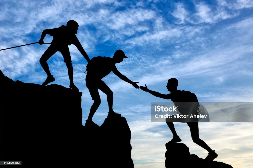Silhouette of two climbers in the mountains help another climber Silhouette of two climbers in the mountains help another climber. Conceptual image teamwork Mountain Climbing Stock Photo
