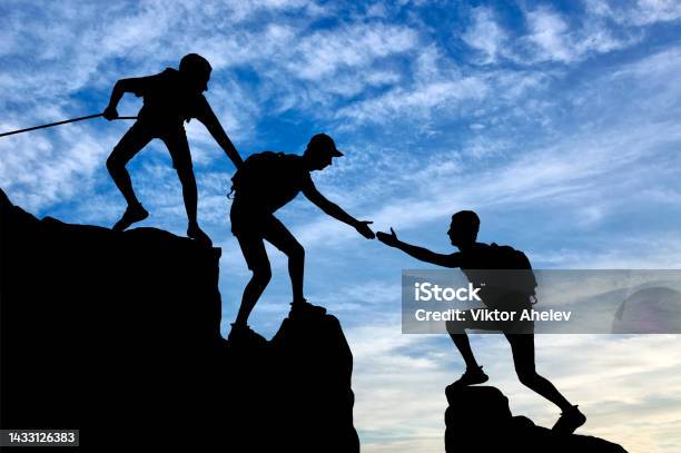 Silhouette Of Two Climbers In The Mountains Help Another Climber Stock Photo - Download Image Now