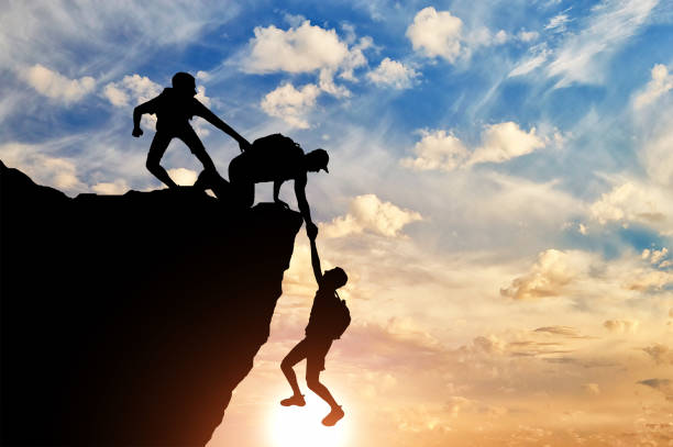 istock Silhouette of three male climbers rescuing another male climber pulling his arm 1433126406