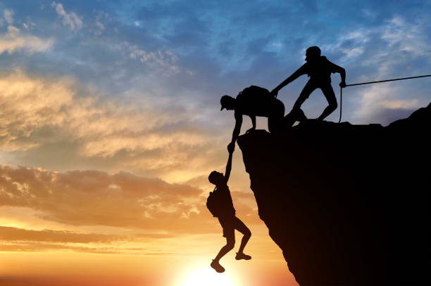 istock Silhouette of three male climbers rescuing another male climber pulling his arm 1433126415