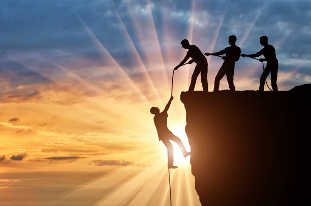 istock Silhouette of three climbers pulling out of the cliff of a man. 1433126422