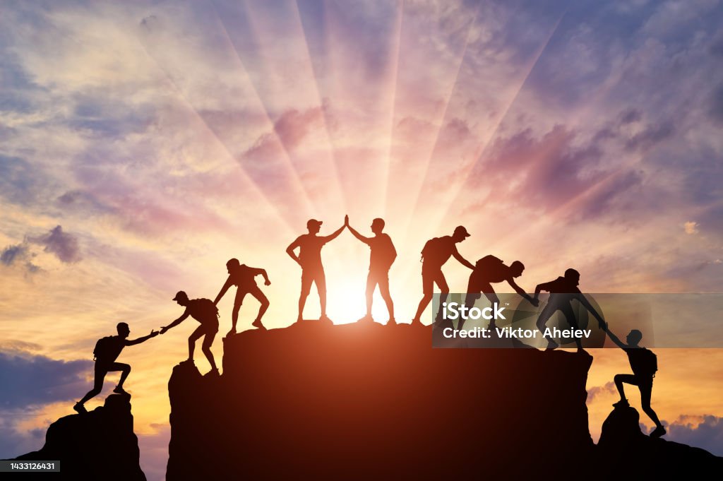 Silhouette of climbers who climbed to the top of the mountain thanks to mutual assistance and teamwork Silhouette of climbers who climbed to the top of the mountain thanks to mutual assistance and teamwork. Conceptual scene of a team of alpinists Teamwork Stock Photo