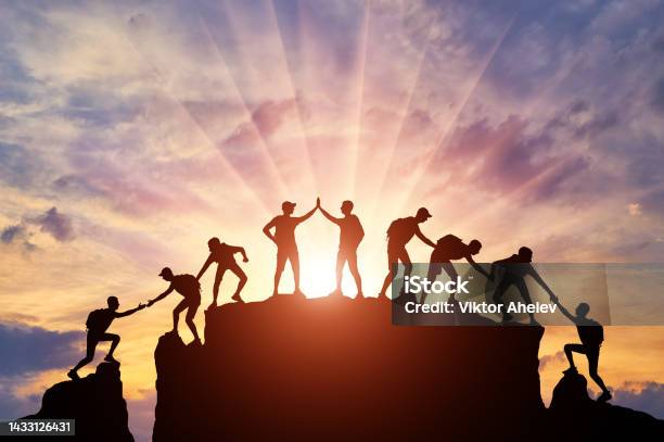 Silhouette Of Climbers Who Climbed To The Top Of The Mountain Thanks To Mutual Assistance And Teamwork Stock Photo - Download Image Now