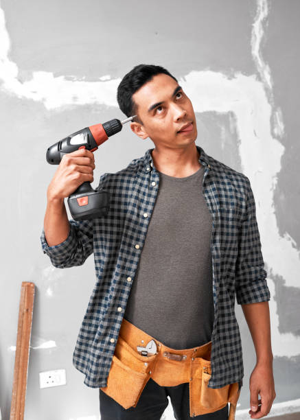 istock A young Asian man holds drill to head pulling silly face while sick of home DIY 1433127471