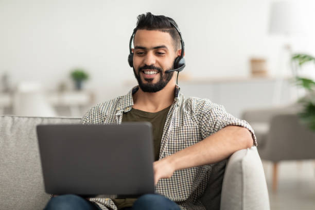 istock Young happy Arab man in headphones using laptop pc, working online from home 1433131570