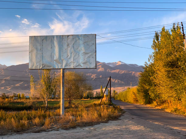 road to the mountains in autumn sunset light with an empty bilboard in the foreground - vibrant color rural scene outdoors tree imagens e fotografias de stock