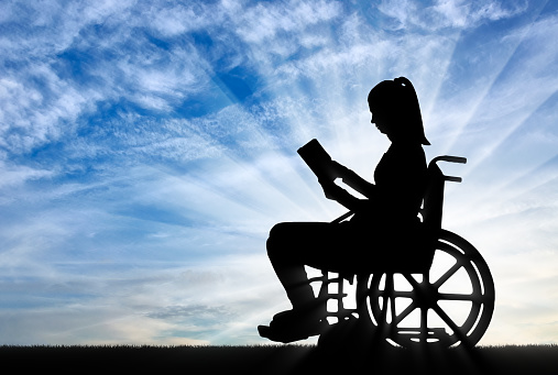 Silhouette of a disabled woman in a wheelchair reading a book in the fresh air. Concept of the way of life of people with disabilities