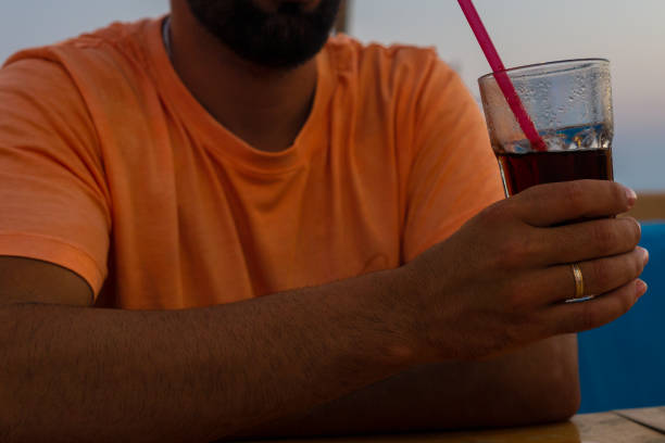 istock Young man leaning on a bar table while holding a glass with a soft drink and a straw in one hand. 1433133256