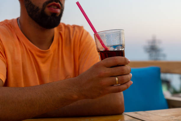 istock Young man leaning on a bar table while holding a glass with a soft drink and a straw in one hand. 1433133288