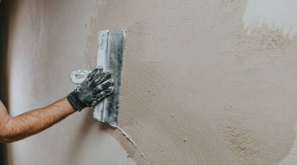 Builder in work overalls plastering a wall indoor Male builder in work overalls plastering a wall using a construction trowel. Horizontal panorama banner with blank space for text. hand with a plaster spatula stock pictures, royalty-free photos & images