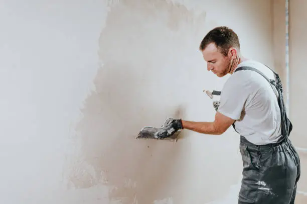 Male builder in work overalls plastering a wall using a construction trowel. Horizontal panorama banner with blank space for text.