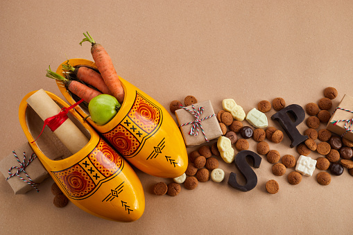 Saint Nicholas - Sinterklaas day with shoe, carrot and traditional sweets on caramel background.