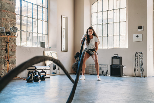 A woman is doing exercises with a rope at the gym. Cross training exercise.