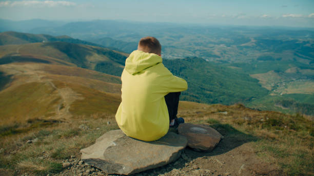 istock Young guy sitting on stone and watching on landscape 1433137495