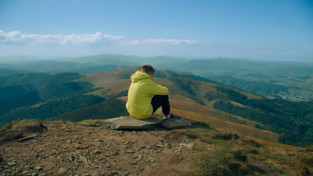 istock Young guy sitting on stone and watching on landscape 1433137559