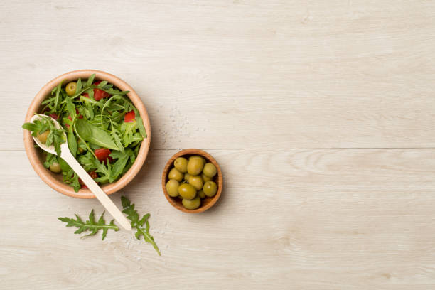 Fresh salad with arugula, spinach and vegetables on wooden background, top view.