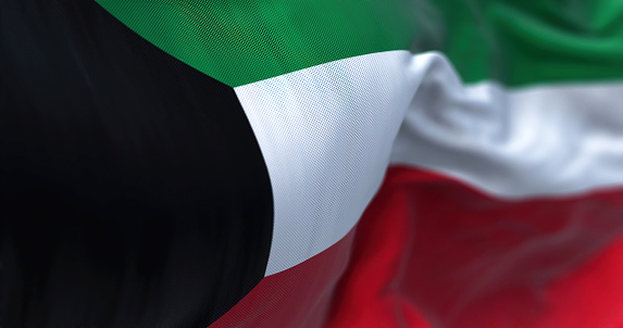 Close-up view of the Kuwait national flag waving in the wind. The State of Kuwait is a country in Western Asia. Fabric textured background. Selective focus