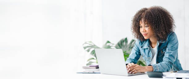노트북과 함께 흰색 사무실에 앉아있는 미국 십대 여성, 그녀는 집에서 노트북으로 온라인으로 공부하는 학생, 온라인으로 공부하는 대학생, 온라인 웹 교육 개념입니다. - internet success household equipment horizontal 뉴스 사진 이미지