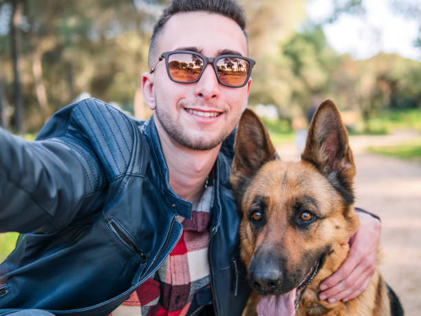 Young man taking a photo with his dog in the forest. Selective focus.
