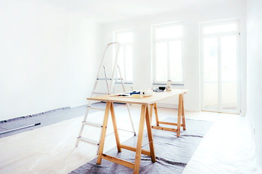 Painting walls of an empty room. Empty room of an apartment during restoration with tools on wooden table and ladder.