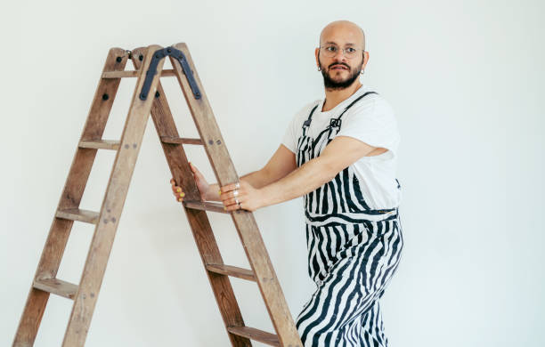 Young man climbing up the ladder while painting interior walls at home. Handsome young man renovating of his home.