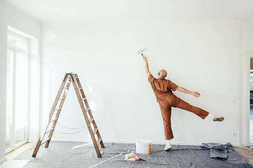 Rear view of a young man coloring wall of the living room with paint roller. Man having fun doing renovations at home.