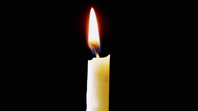 Burning White Candle with a Bright Flame on an Isolated Black Background. Zoom