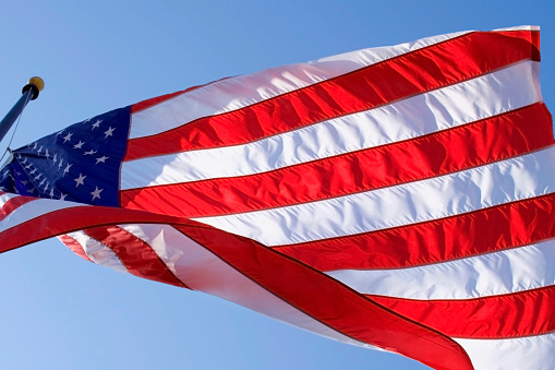 Waving big flag of United States of America on blue sky background