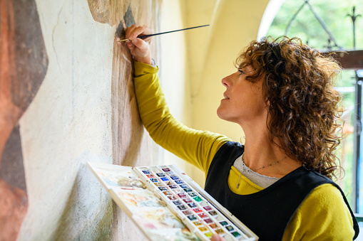 Professional restorer restoring antique chapel fresco in Italy