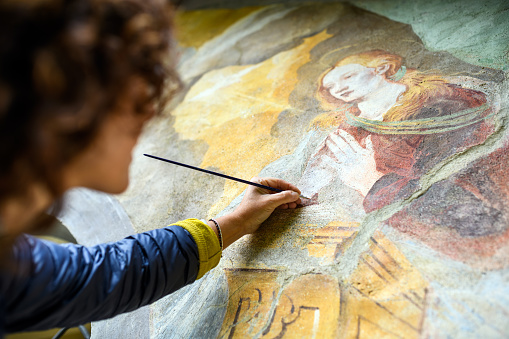 Professional restorer restoring antique chapel fresco in Italy