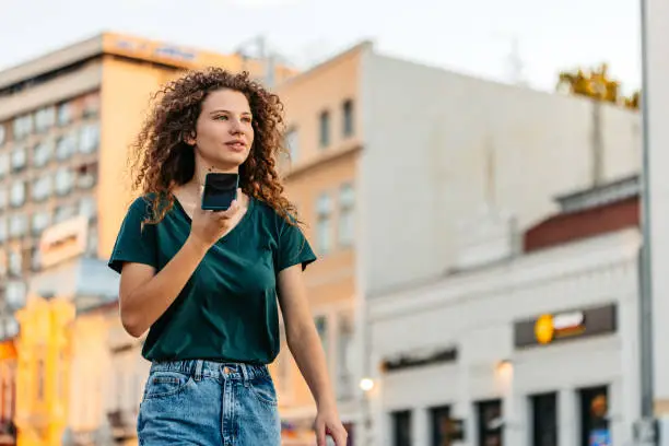 Photo of Young Woman Sending A Voice Message While Walking Down The Street