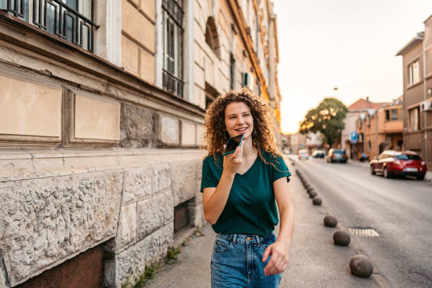 young woman sending a voice message while walking down the street - vocoder imagens e fotografias de stock