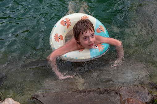 A little boy learns to swim with the help of a lifebuoy in the summer in the village in the pond next to the house