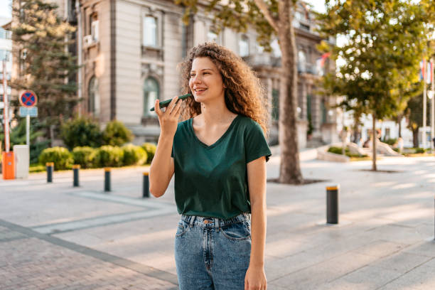 young woman sending a voice message while walking down the street - vocoder imagens e fotografias de stock