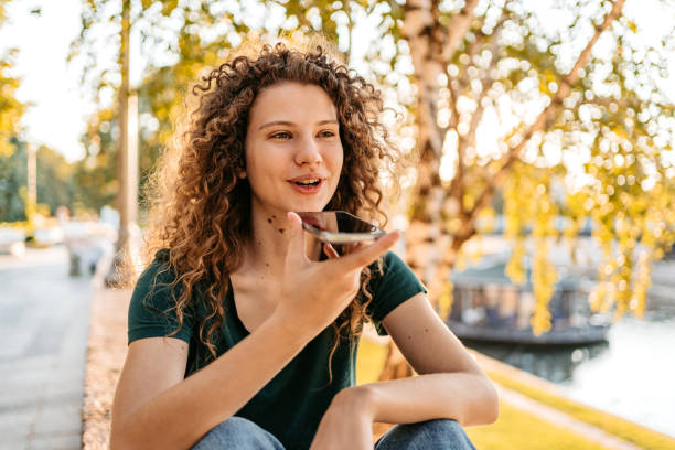 Young Woman Sending A Voice Message While Sitting On The Quayside Beautiful young woman sending a voice message while sitting on the quayside. snapschat stock pictures, royalty-free photos & images