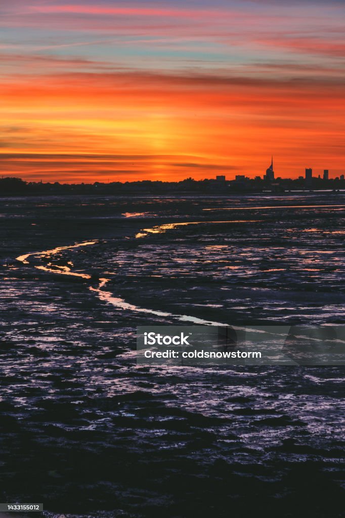 Sunset on Hayling Island looking towards Portsmouth city skyline A dramatic glowing sunset on the English south coast at Hayling Island, looking across to the city skyline of Portsmouth, including the distinctive shape of the Spinnaker Tower. Beach Stock Photo