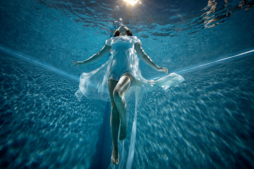 Conceptual underwater image of a woman with a white dress while floating towards the surface.