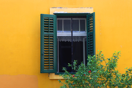 Traditional Mediterranean window with green shutters and bright yellow wall. Picturesque architecture in Split, Croatia.
