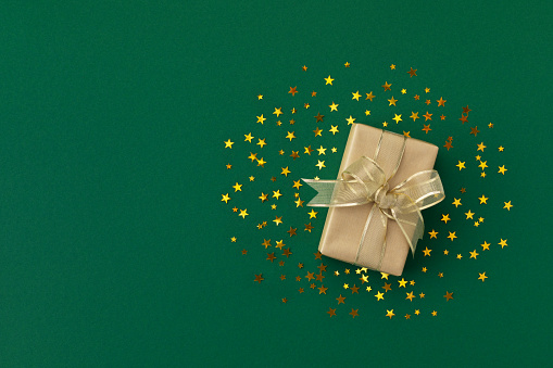 Christmas gift or present and golden star confetti on green table top view. Christmas greeting card with holiday decorations.