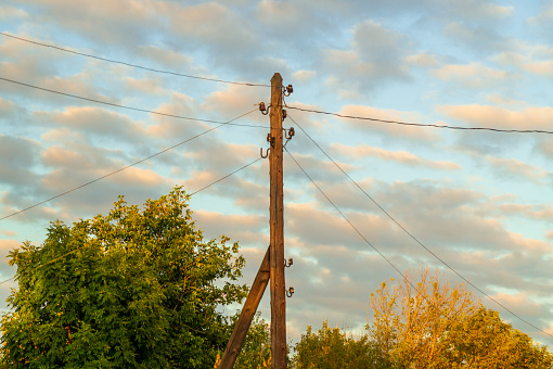 Old electric pole with wires in the village at sunset. Background of a beautiful sky.