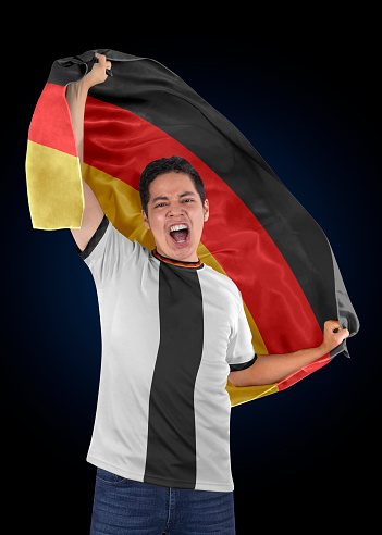 Soccer fan with the flag of his country Germany and jersey shouting with emotion for the victory of his team on a black background.