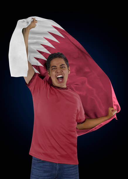 Soccer fan with the flag of his country Qatar and jersey shouting with emotion for the victory of his team on a black background.