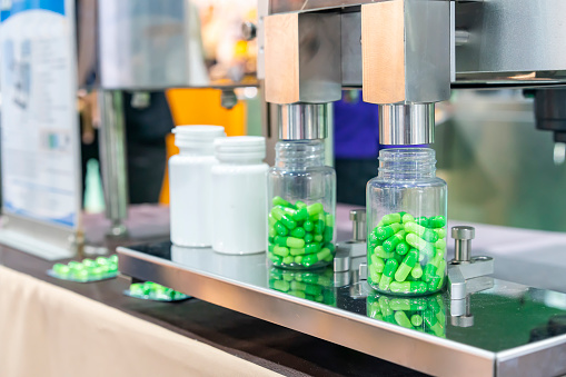 close up transparent plastic bottle under nozzle dispenser component of automatic medicine capsule bottle filling and counting machine during manufacturing process