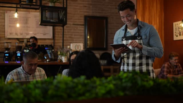 Waiter using digital tablet taking order from customers at a restaurant