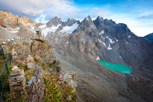 Old stone bell tower high Alps mountains ridge cliff glacier lake, Refuge Marinelli Bombardieri mountaineering tourism, Italy travel Europe.