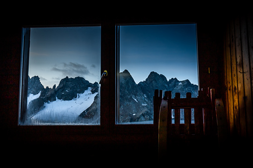 Through window evening dusk alpine peaks mountains ridge range glacier view. Italian Alps, Refuge Marinelli Bombardieri mountain hut, Europe tourism travel.