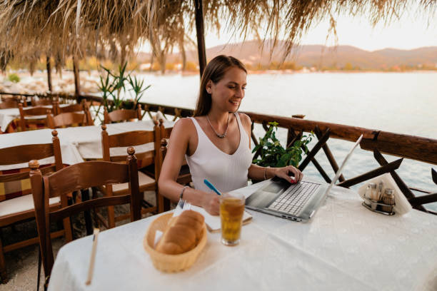 istock Smiling woman using a laptop in a seaside restaurant in Greece 1433174991