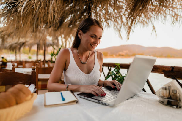 mujer aprendiendo y usando una computadora portátil en un restaurante a la orilla del mar - travel red vacations outdoors fotografías e imágenes de stock